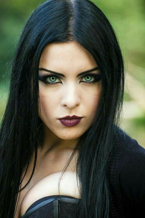 Mujer con ropa estilo gótico, con grandes ojos verdes, labios pintados de negro y pelo largo negro. Viste un corsét y chaqueta negras.